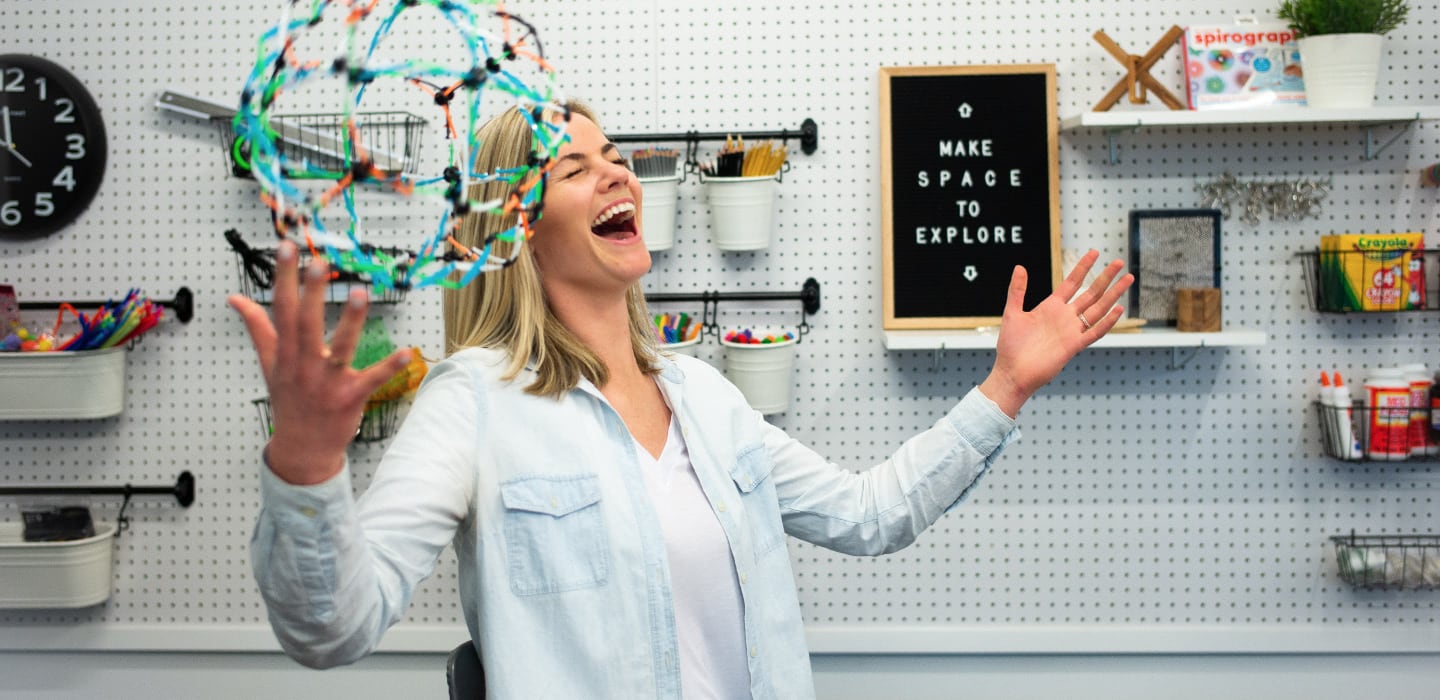 Femme en train de rire qui joue avec une sphère Hoberman dans un espace de création.